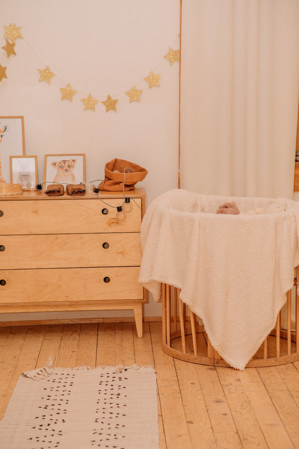 image d'une chambre pour bébé avec une commode et un petit landau circulaire, le tout en bois clair et avec une guirlande d'étoiles accrochée au mur.